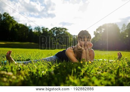 Portrait of sporty young woman practicing yoga, doing upavishta konasana, stretching looking at camera and smiling on sea shore in summer