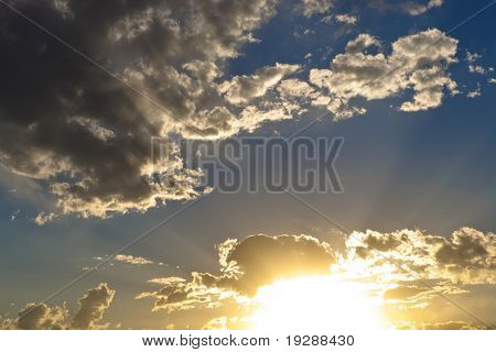 Vibrant sunset with sunbeams across blue sky with scattered white clouds