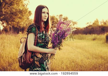 Happy red-haired woman with a bouquet of wildflowers. Village