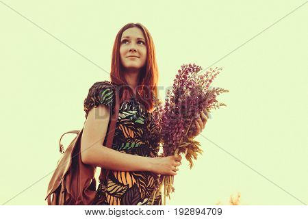 Happy red-haired woman with a bouquet of wildflowers. Village