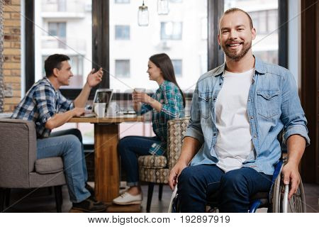 Living life to the fullest. Nice sociable disabled guy enjoying his time while meeting his university friends in a cafe and looking delighted