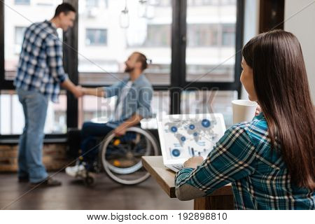 New venture. Supporting charming sociable guy greeting his new colleague who joining their startup and visiting the office for the first time