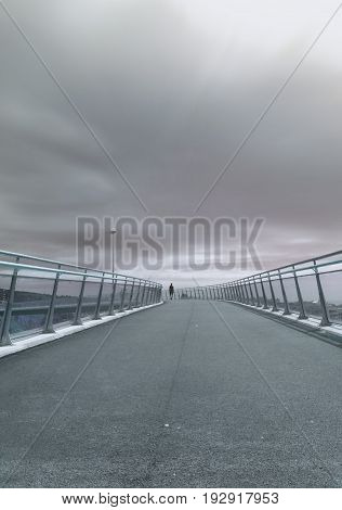 A lonely person walking on a bridge on a cloudy afternoon