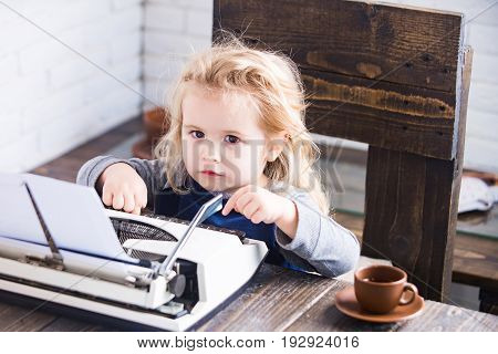 business kid or small businessman child sitting at table and typing typewriter with paper and coffee cup on white brick wall background new technology