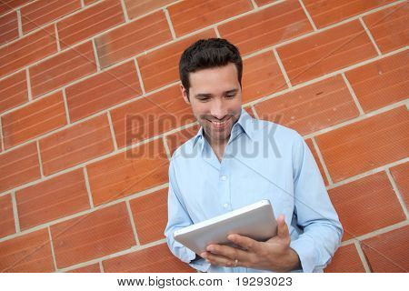 Atraktivní muž pomocí elektronických tabletu se naklonil na brickwall