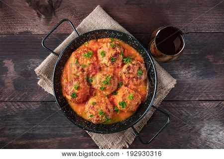 An overhead photo of meatballs in tomato sauce, shot from above in the skillet on dark rustic textures, with a place for text and a glass of red wine
