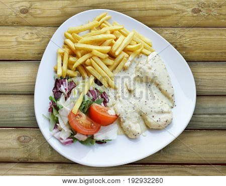 Photo from top of a plate with Aromatic Chicken with chips and mixed salad on a wooden table