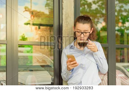 Half Thai half American hold iphone in right hand and glass of hot black coffee in left hand standing against glass door at coffee shopfreelance woman lifestyle concept.