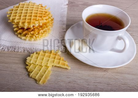 Breakfast With Waffles Stack On Napkin And Pieces Of Waffle With White Cup Of Black Tea On Wooden Su