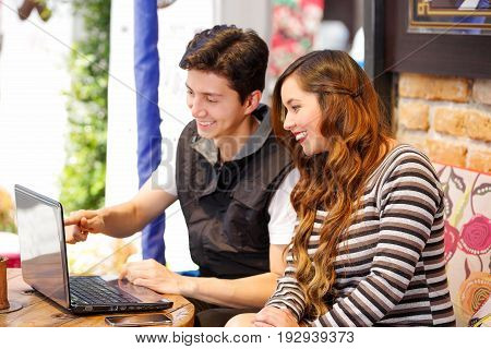 Smiling happy couple at the bar spending time together, while they are working in his computer.
