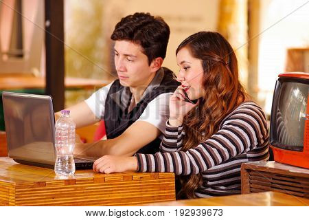 Beautiful couple at the bar spending time together, while he is working in his computer while she is using her cellphone.