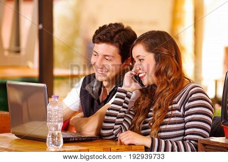 Beautiful couple at the bar spending time together, while he is working in his computer while she is using her cellphone.