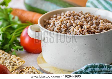 Natural organic food. Boiled buckwheat porridge in pot. Fresh raw vegetables.