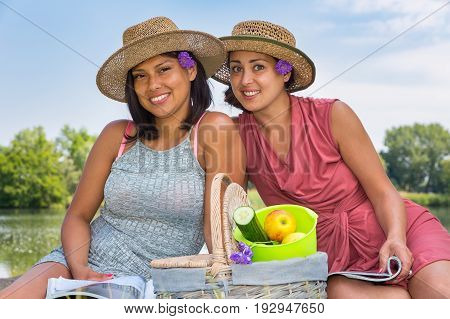 Two friends with hats and picknick basket at water in nature