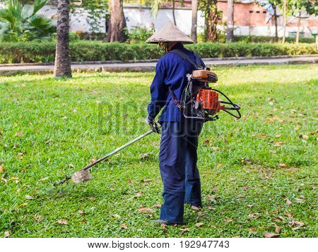 The worker of a garden cuts off a grass. The man in a uniform of the general worker works at a lawn. Work of municipal services on improvement of territories.