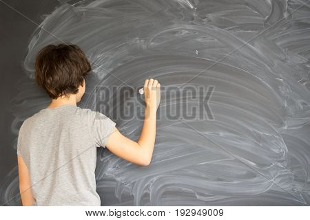 Teenager Boy with chalk in hand writting on empty black board