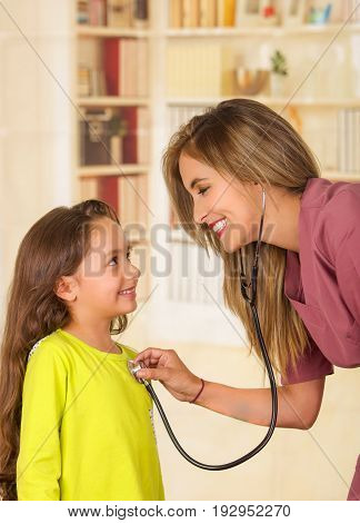 Young pretty girl smiling while a beautiful smiling doctor examining with a stethoscope in her chest in a office background.
