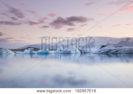 Giant pieces of ice flowing on and reflecting in cold lake with a huge glaciar behind, jokulsarlon glaciar lagoon, Iceland