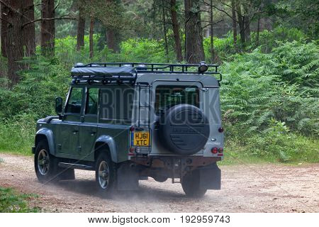 BEAULIEU HAMPSHIRE UNITED KINGDOM - JUNE 25 2017 Land Rover day with many varieties of Land Rovers this Defender is driving on a dusty off road track in the woods.