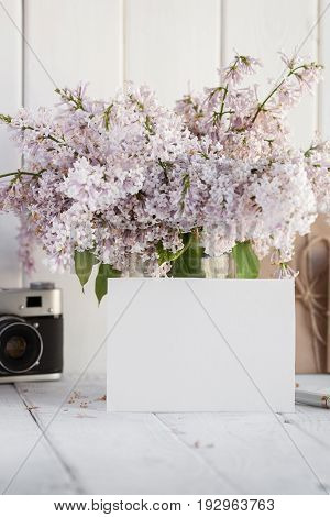 Blank white greeting card with lilac flowers bouquet and envelope with vintage camera on white wooden background. mock up.