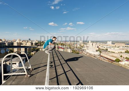 Roofer sits on the railing at the edge of the roof. Extreme life. Courage and adrenaline. Parkour and Rufing.