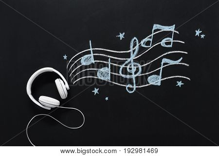 Headphones With Wire And Musical Notes Drawn On Black Chalkboard