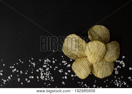 Crinkle cut potato chips on a chalkboard. Tasty spicy potato chips with salt.Top view