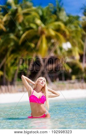 Beautiful girl with long blond hair in bikini on the shore of a tropical beach. Palm trees in the background. Summer vacation concept.