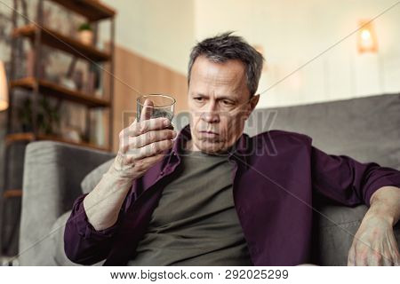 Serious Depressed Man Observing Alcohol In Glass And Deeply Thinking