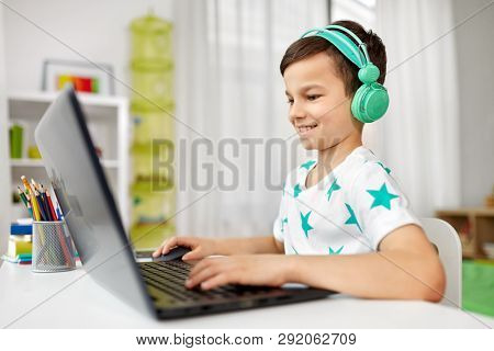 technology, gaming and people concept - boy in headphones playing video game on laptop computer at home