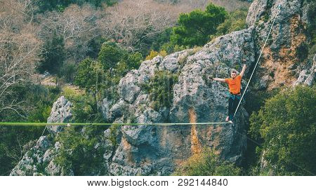 A Man Is Walking Along A Stretched Sling. Highline In The Mountains. Man Catches Balance. Performanc
