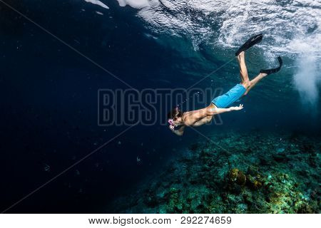 Young man snorkeling and skin diving over the coral reef edge in the tropical sea