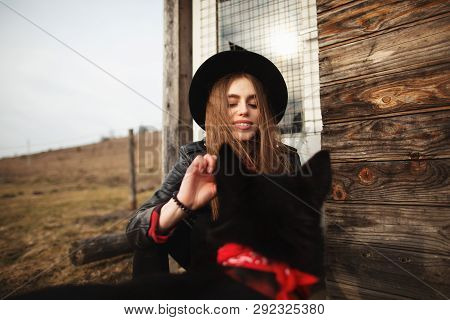 Girl Feeds Her Black Dog Brovko Vivchar In Fron Of Old Wooden House.
