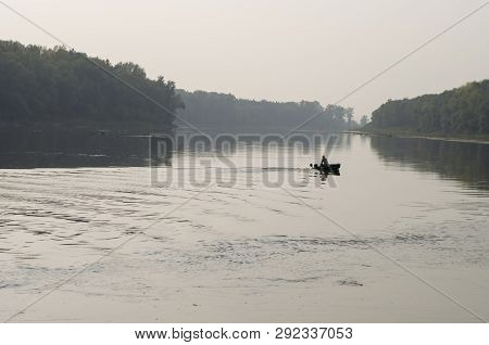 Fisherman Are Swiming On The Boat. Wide River Flowing Across Green Forest. Fall. Evening. Reflection