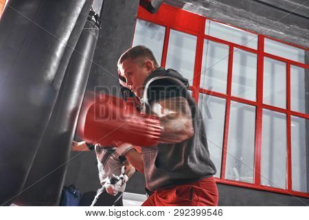 Ready To Break His Record. Young Muscular Athlete In Sports Clothing Training Hard On Heavy Punch Ba