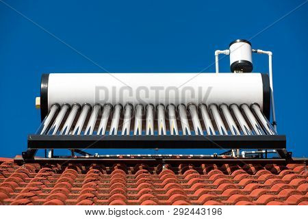 Solar Water Heater Boiler On Residentual House Rooftop, Perfect Blue Sky Background.
