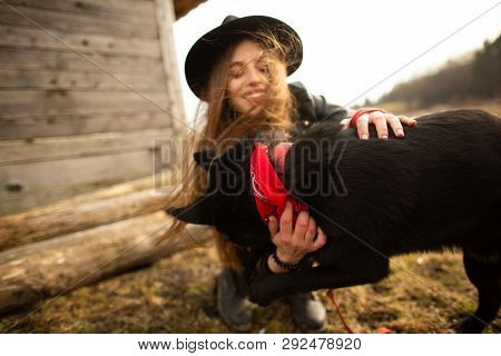Happy Young Woman Plaing With Her Black Dog Brovko Vivchar In Fron Of Old Wooden House.
