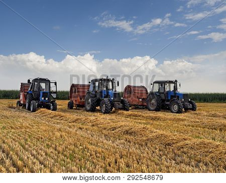 Three Wheeled Tractors With Roll Balers On A Sloping Wheat Field