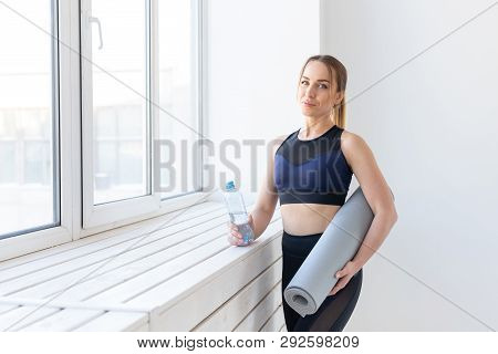 People, Sport And Fitness Concept - Young Woman With Yoga Mat And Bottle Of Water Standing Near Wind