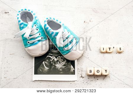 Blue Baby Booties With A Picture Of Ultrasound For 20 Weeks On A Light Background. Inscription Its B