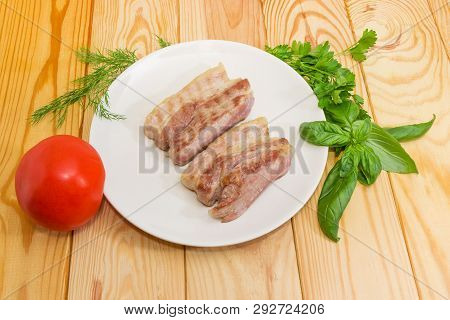 Two Slices Of The Grilled Streaky Bacon On The White Dish, Fresh Tomato And Different Greens On A Wo