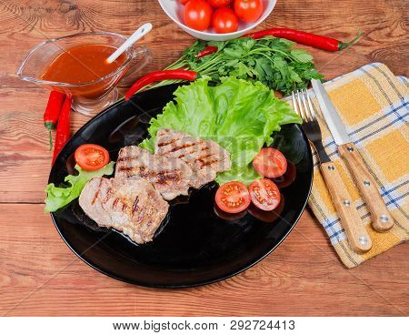Top View Of The Grilled Pork Steaks On Lettuce Leaves And Cherry Tomatoes On Black Dish, Souce, Gree
