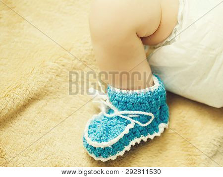 Blue Knit Childrens Bootee With White Bow On Small Baby Foot On Yellow Blanket