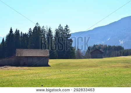 Panoramic Photo Of The Bavarian Mountains Behind A Hut In Spring.