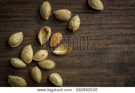 Close up of an almod seed cracked open from a shell, scattered on wooden background. Top view of almond seeds with its shell.