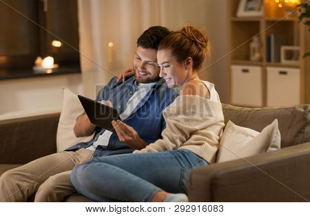 technology, internet and people concept - happy couple using tablet computer at home in evening