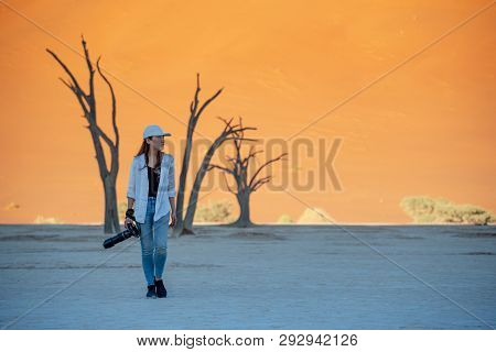 Young Asian Woman Photographer And Traveler Walking On Clay Pan Near Dead Trees In Deadvlei (sossusv