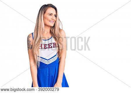 Young beautiful blonde woman wearing cheerleader uniform looking away to side with smile on face, natural expression. laughing confident. 