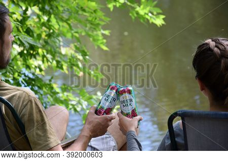 Young Boy And Girl Cheers With Beermix Bewerage Tin Cans Outdoors During Fishing. Beermix Is Product