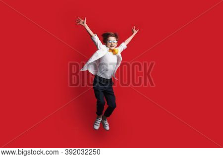 Caucasian Boy With Headphones Is Jumping On A Red Studio Wall Holding Up The Arms And Looking At Cam